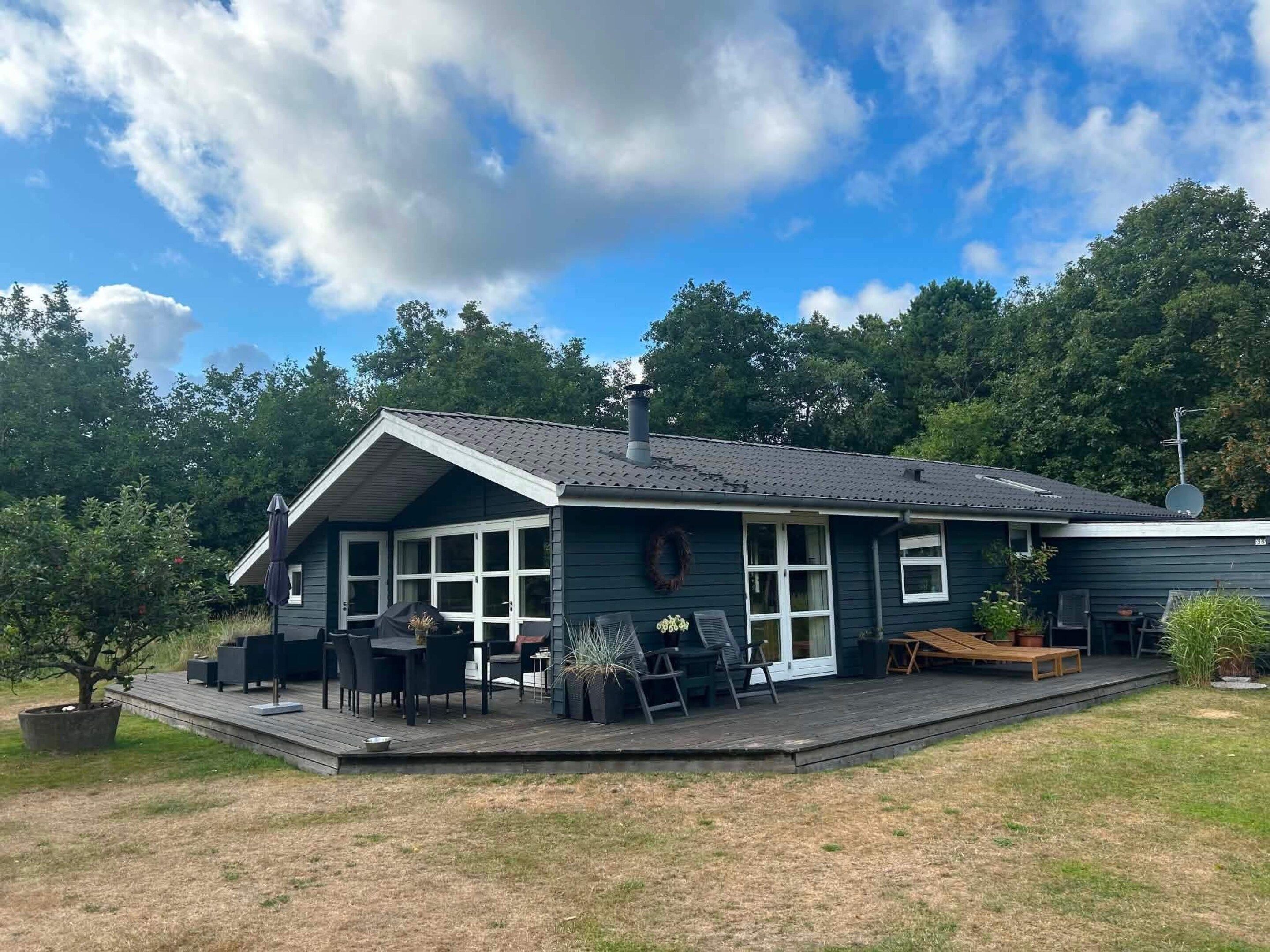 Ein zweistöckiges Haus mit einer Terrasse, Gartenmöbeln und einer Satellitenschüssel.