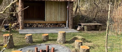 A rustic cabin with a wooden deck, a fire pit, and a bench.
