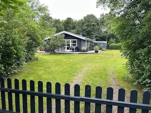 Ein modernes Haus mit überdachter Terrasse, umgeben von einem gepflegten Rasen und üppiger Bepflanzung.