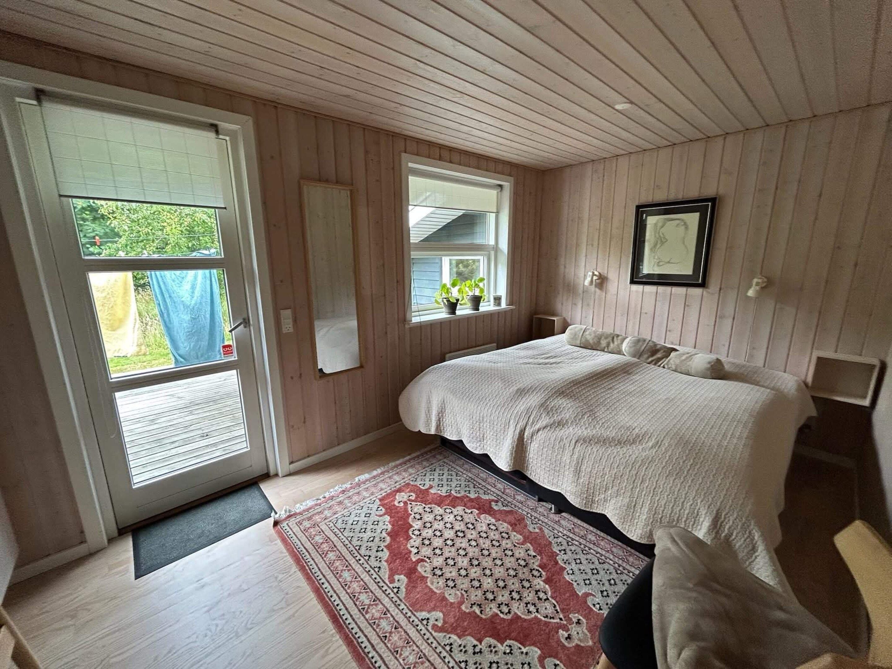 A bedroom with a large bed, a window with a view of greenery, and a door leading outside.