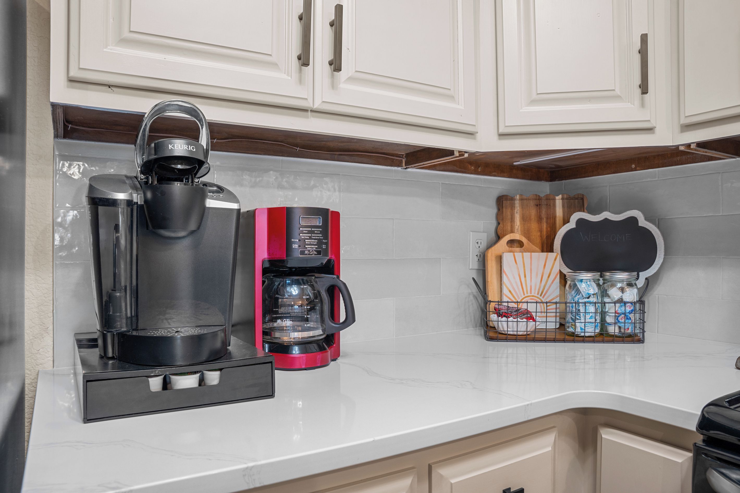 A kitchen with a coffee maker, a kettle, and a coffee grinder on the counter.