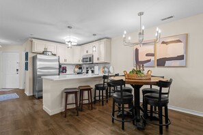 Eine moderne Küche mit weißen Schränken, Edelstahlgeräten und einem Essbereich mit einem Holztisch und schwarzen Stühlen.