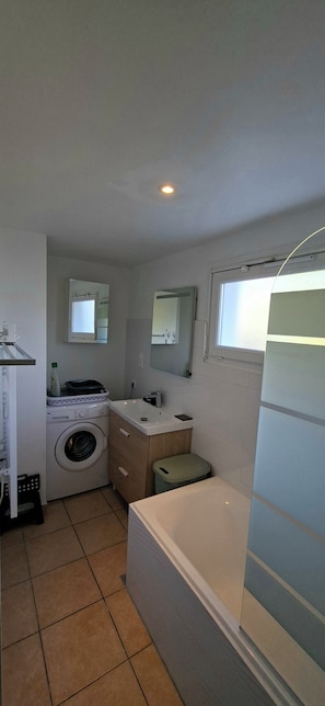 A compact bathroom with a washing machine, a sink, a mirror, and a bathtub. - Vrbo Property (Saint-Évarzec)