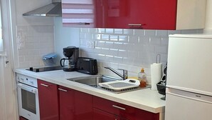 Eine Küche mit roten Schränken, einer weißen Arbeitsplatte, einem Herd, einem Spülbecken und einem Kühlschrank.