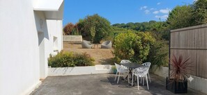 A patio with a table and chairs, surrounded by greenery and a wooden fence. - Vrbo Property (Saint-Évarzec)