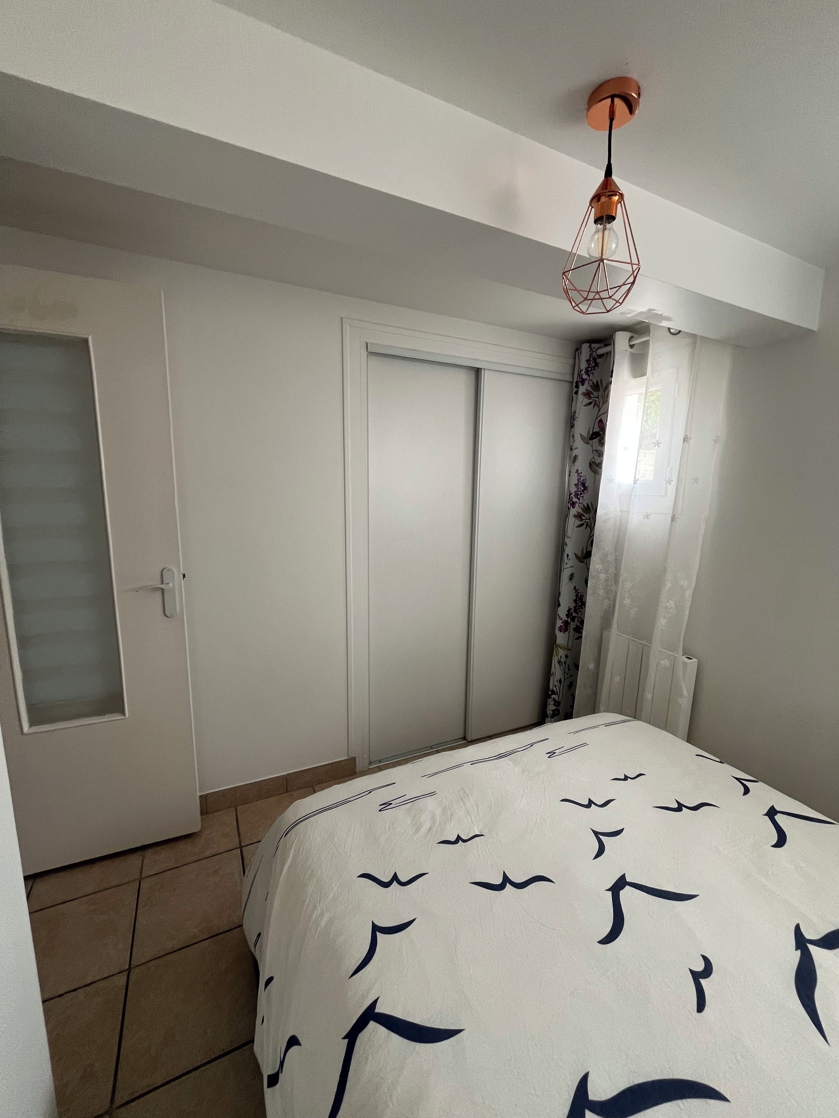A bedroom with a bed, a wardrobe, a door with a frosted glass panel, and a hanging light fixture.