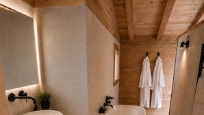 A modern bathroom with a freestanding bathtub, a large mirror, and wooden shelving with towels. - SIGA Grand BO Chalet, Sleeps 14–16 — Newly Built and Fully Equipped (Le Grand-Bornand)