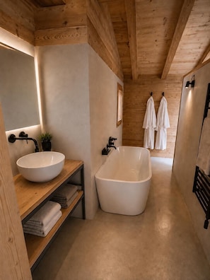 A modern bathroom with a freestanding bathtub, a large mirror, and wooden shelving with towels. - SIGA Grand BO Chalet, Sleeps 14–16 — Newly Built and Fully Equipped (Le Grand-Bornand)
