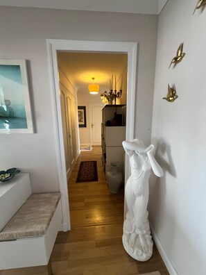 Un pasillo con un banco blanco, una estatua y una puerta que da a otra habitación.
