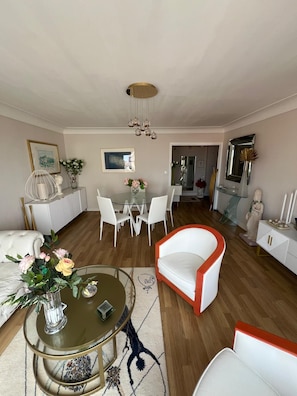 Uma sala de estar moderna com uma mesa de vidro redonda, cadeiras brancas, uma poltrona vermelha e branca e um candelabro.