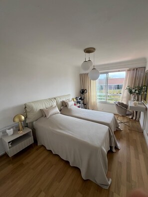 Ein Schlafzimmer mit zwei Betten, einem Schreibtisch, einem Stuhl und einem Fenster mit Vorhängen.