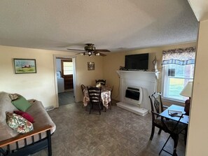 A living room with a fireplace, a ceiling fan, a dining area, and a television. - Happy Homeplace - 1-bedroom farmhouse with AC in charming Bedford (Bedford)