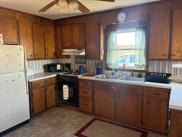 Cocina con armarios de madera, un refrigerador, un microondas, un lavamanos y una ventana con cortinas.