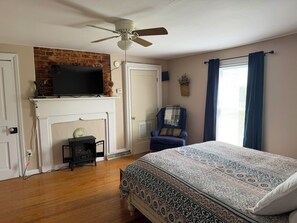 A bedroom with a bed, a television on a mantel, a fireplace, a chair, and a window with curtains. - Happy Homeplace - 1-bedroom farmhouse with AC in charming Bedford (Bedford)