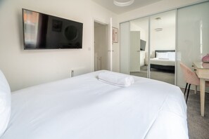 A hotel room with a bed, a television mounted on the wall, a desk with a chair, and a sliding door leading to another room. - Broomsfield House |2 Bed | Parking |UEA | Hospital (Norwich)