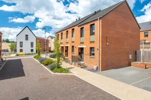 A residential building with a brick facade, a flat roof, and a small front garden with a bench. - Broomsfield House |2 Bed | Parking |UEA | Hospital (Norwich)