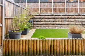 A fenced backyard with a small lawn, two potted plants, and a wooden fence. - Broomsfield House |2 Bed | Parking |UEA | Hospital (Norwich)