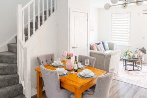 A dining area with a wooden table set for four, grey upholstered chairs, and a staircase with white railings. - Broomsfield House |2 Bed | Parking |UEA | Hospital (Norwich)