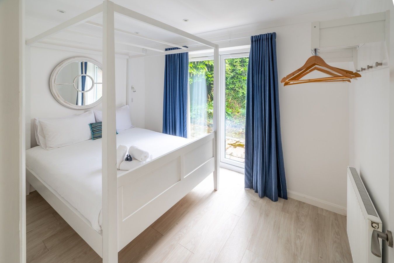 Une chambre à coucher avec un lit à baldaquin, un miroir rond et une vue sur la verdure environnante.