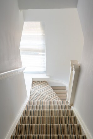 A staircase with striped carpet leading to a window with blinds. - Swift Host | Scriveners | Blakeney | Sleeps 12 | Pet Friendly | Free Parking (Blakeney)