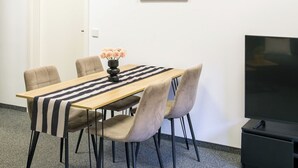 Et mødelokale med et langt bord, seks stole, en vase med blomster, et billedværk på væggen og et fjernsyn.
