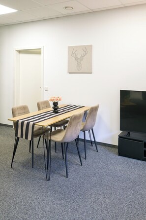Ein Konferenzraum mit einem langen Tisch, sechs Stühlen, einer Blumenvase, einem Wandbild und einem Fernseher.