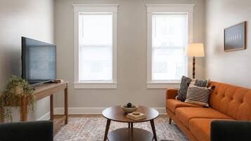 A living room with a television, two windows, a sofa, a table with a bowl, and a lamp.