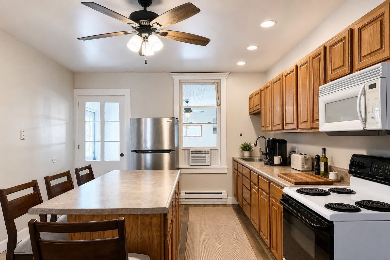A modern kitchen with a central island, wooden cabinets, a stainless steel refrigerator, a microwave, and a stove.