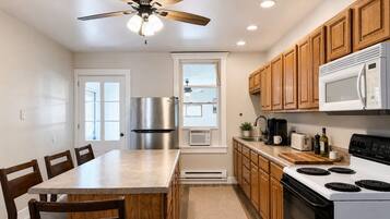A modern kitchen with a central island, wooden cabinets, a stainless steel refrigerator, a microwave, and a stove.
