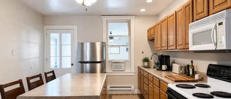 A modern kitchen with a central island, wooden cabinets, a stainless steel refrigerator, a microwave, and a stove.