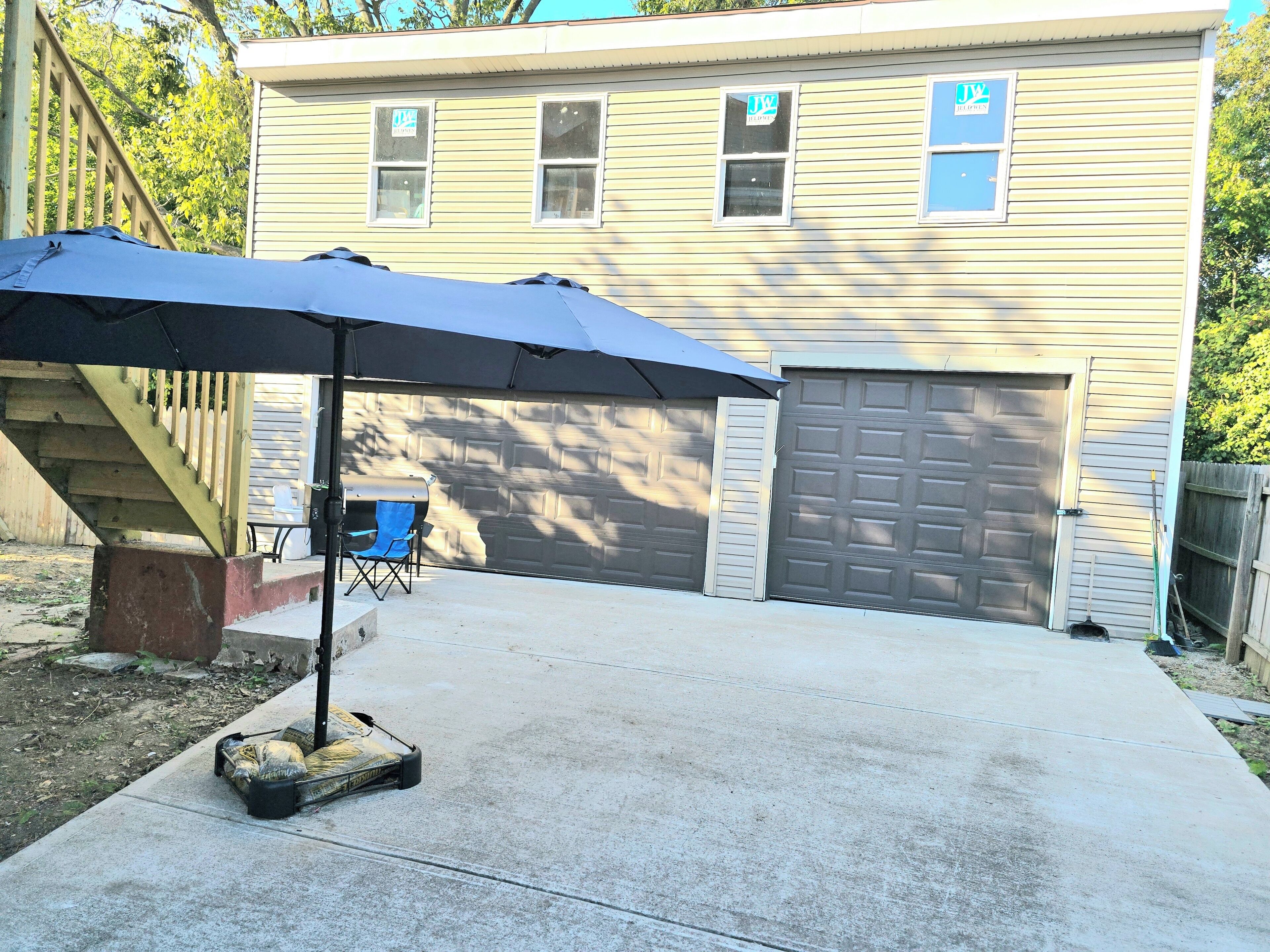 A residential garage with a covered patio area, a barbecue grill, and a blue folding chair.