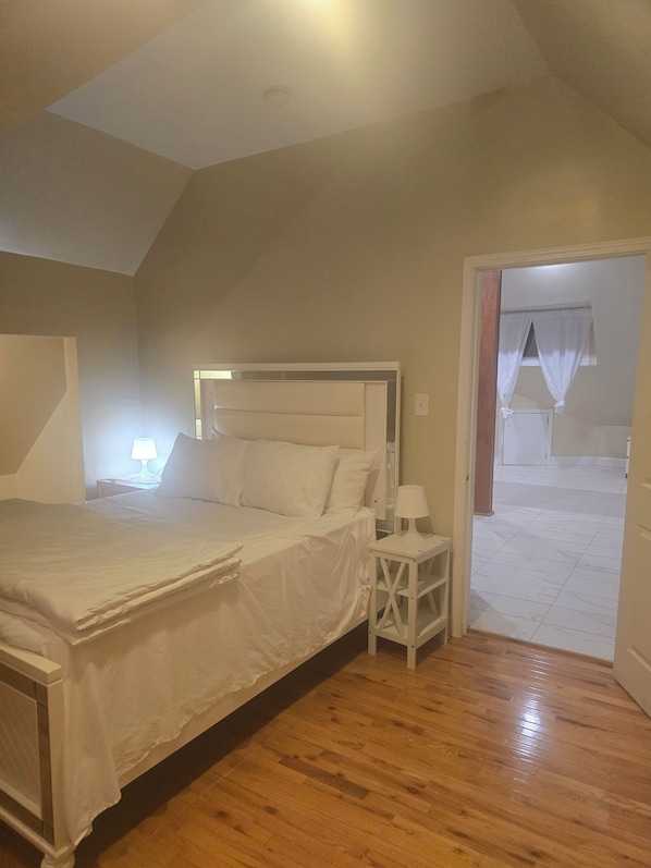 A bedroom with a bed, bedside tables, and a door leading to another room.