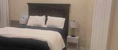 Un dormitorio con una cama de madera oscura, ropa de cama blanca, dos lámparas de noche y un suelo de baldosas.