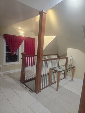 A staircase with a wooden railing, a glass table, and red curtains.