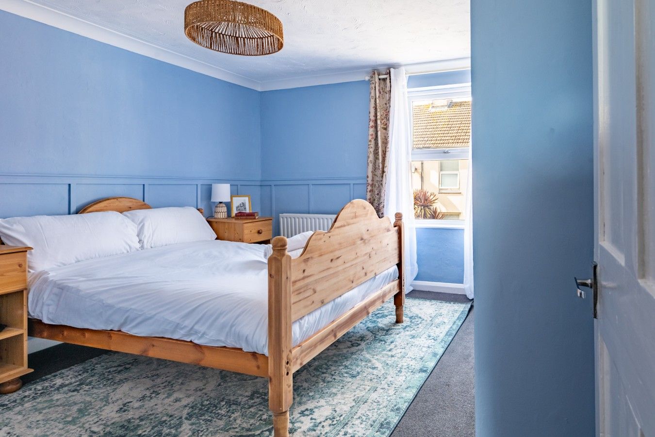 A bedroom with a wooden bed, a nightstand, a lamp, and a view of the outside.