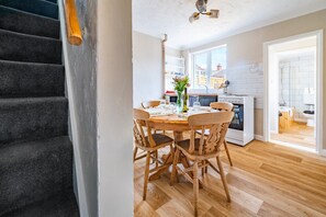 Una cocina moderna con armarios blancos, un comedor con sillas de madera y una escalera con alfombra oscura.