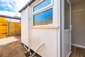 Eine weiße Außenwand mit Fenster, einer Tür und einem Holzzaun im Hintergrund.