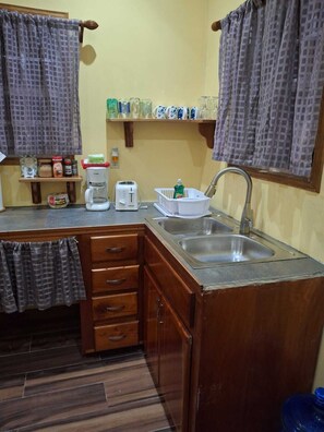 A compact kitchen with a sink, a coffee maker, a toaster, and a small shelf with jars. - Cozy 2-bedroom cottage in awesome Caye Caulker with AC (Caye Caulker)