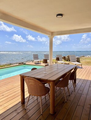 A wooden deck with a pool, lounge chairs, and a table with chairs, overlooking the ocean. - SEA VIEW TINTAMARRE Villa – Brand-new waterfront villa in Oyster Pond (Oyster Pond)