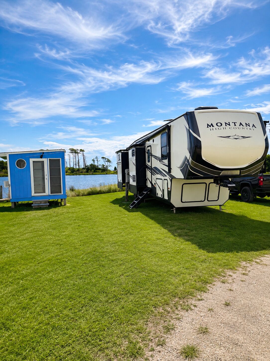 A Montana High Country RV parked on a grassy field with a body of water and trees in the background.