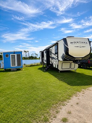 A Montana High Country RV parked on a grassy field with a body of water and trees in the background.