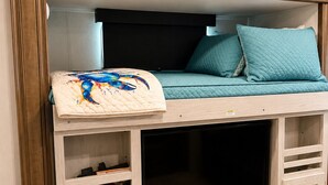 Una cama litera con televisión, armarios de almacenamiento y una colcha decorativa.