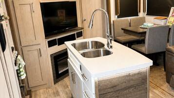A compact kitchen with a built-in sink, wooden cabinets, and a television.