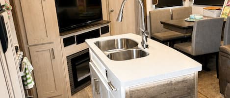 A compact kitchen with a built-in sink, wooden cabinets, and a television.