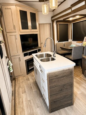 A compact kitchen with a built-in sink, wooden cabinets, and a television.