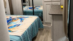 Un dormitorio compacto con dos camas, un pequeño rincón de cocina y un armario con puerta corredera.