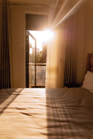 Quarto de hotel com cama, cortinas e vista para o exterior através de uma porta de vidro.