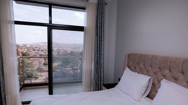 Een hotelkamer met een groot bed, uitzicht op een stadslandschap via een balkon en een raam met gordijnen.