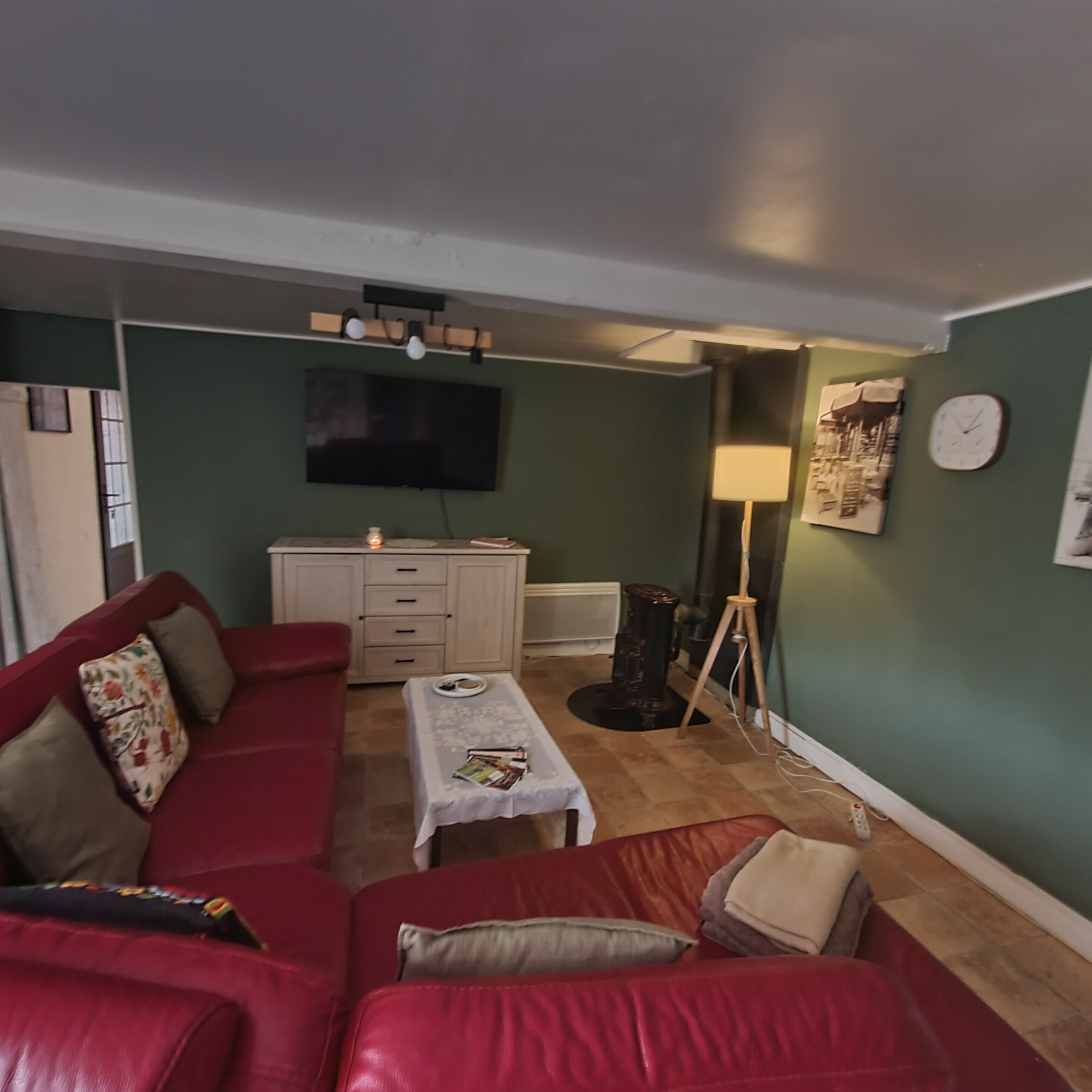 Een woonkamer met een rode bank, een kleine tafel, een televisie en een lamp.