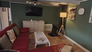 Ein Wohnzimmer mit einem roten Sofa, einem kleinen Tisch, einem Fernseher und einer Lampe.